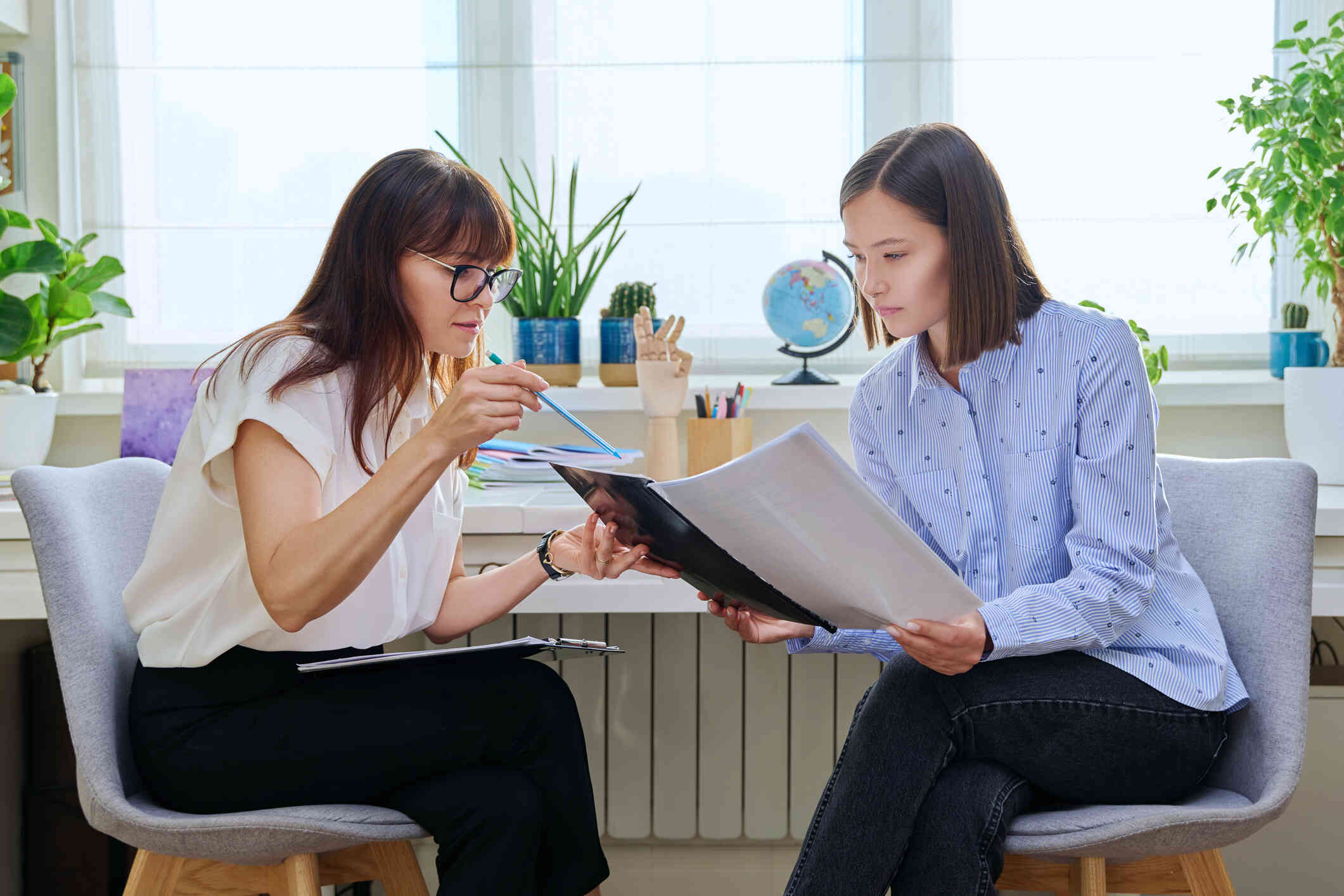 A female therapist points out some information in a book that her female patient is holding in her hands.